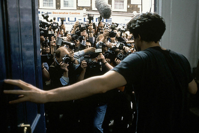 Hugh Grant as William Thacker opens a door to face a large crowd of paparazzi with cameras in a scene from "Notting Hill."