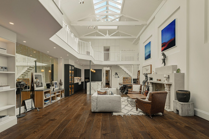 A spacious, modern living area with high ceilings, skylights and exposed beams. Features include dark wood floors, contemporary furniture, abstract art and sculptures.