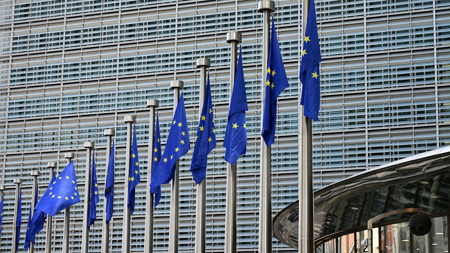European Union flags flutter on flagpoles in front of the Berlaymont building, headquarters of the European Commission.