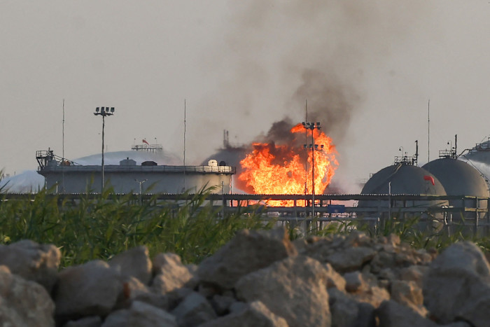 Flames and thick smoke rise from storage tanks at an Aramco oil facility, with industrial structures in the foreground.