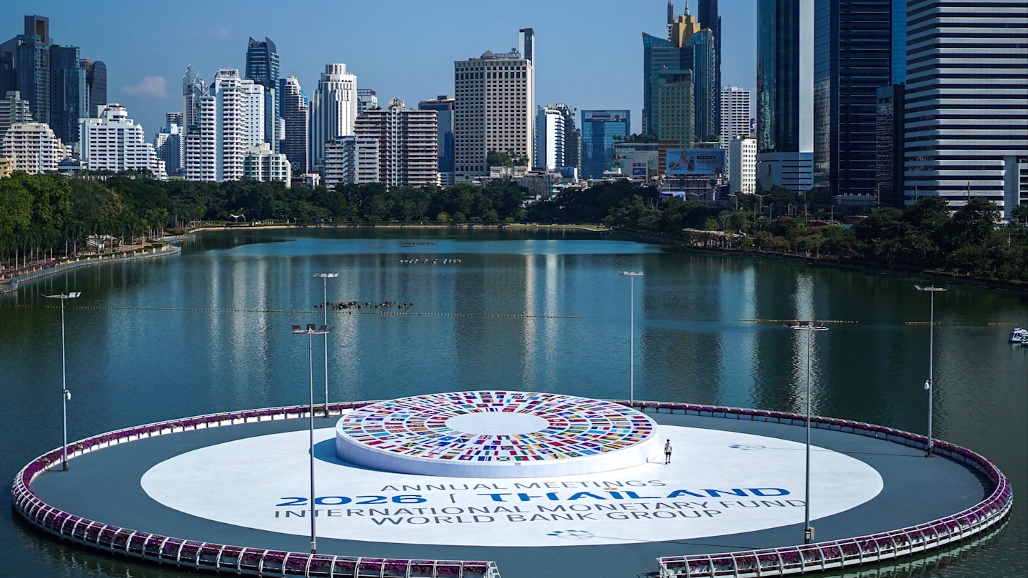 A person stands on a circular platform in a lake with the 2026 IMF-World Bank Annual Meetings logo surrounded by Bangkok’s skyline