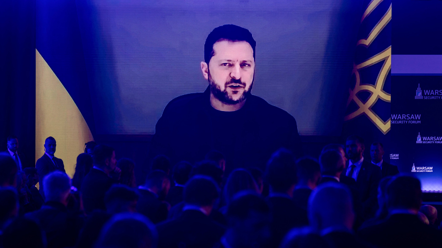 Volodymyr Zelenskyy appears on a large screen speaking via video link to an audience at the Warsaw Security Forum.