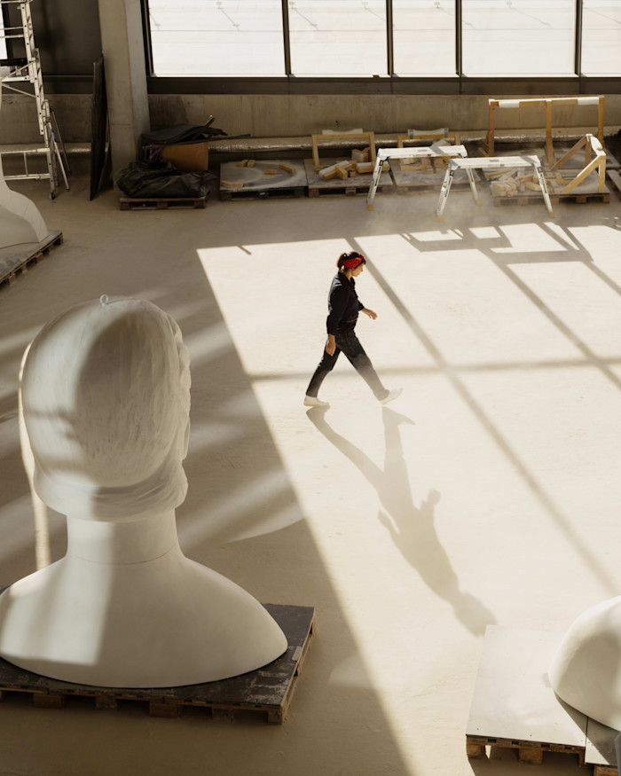 Prune Nourry walks through her studio, passing large sculpted busts and casting a long shadow on the floor.
