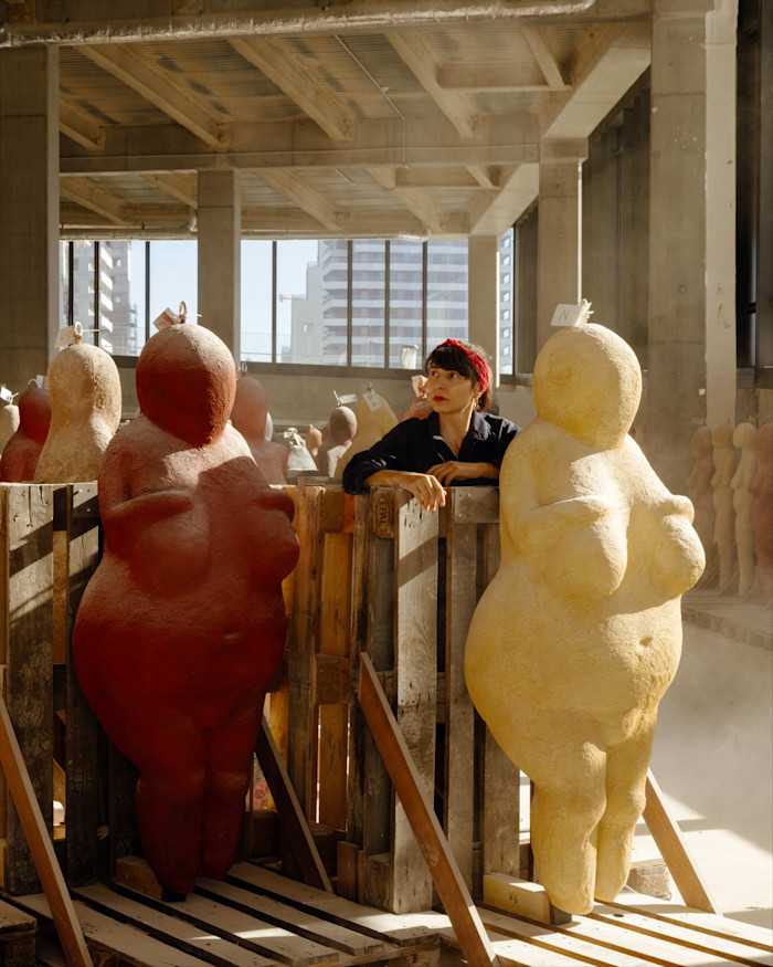 Prune Nourry stands in her Paris studio among large, rounded Venus sculptures from her ongoing series, one red and one yellow.