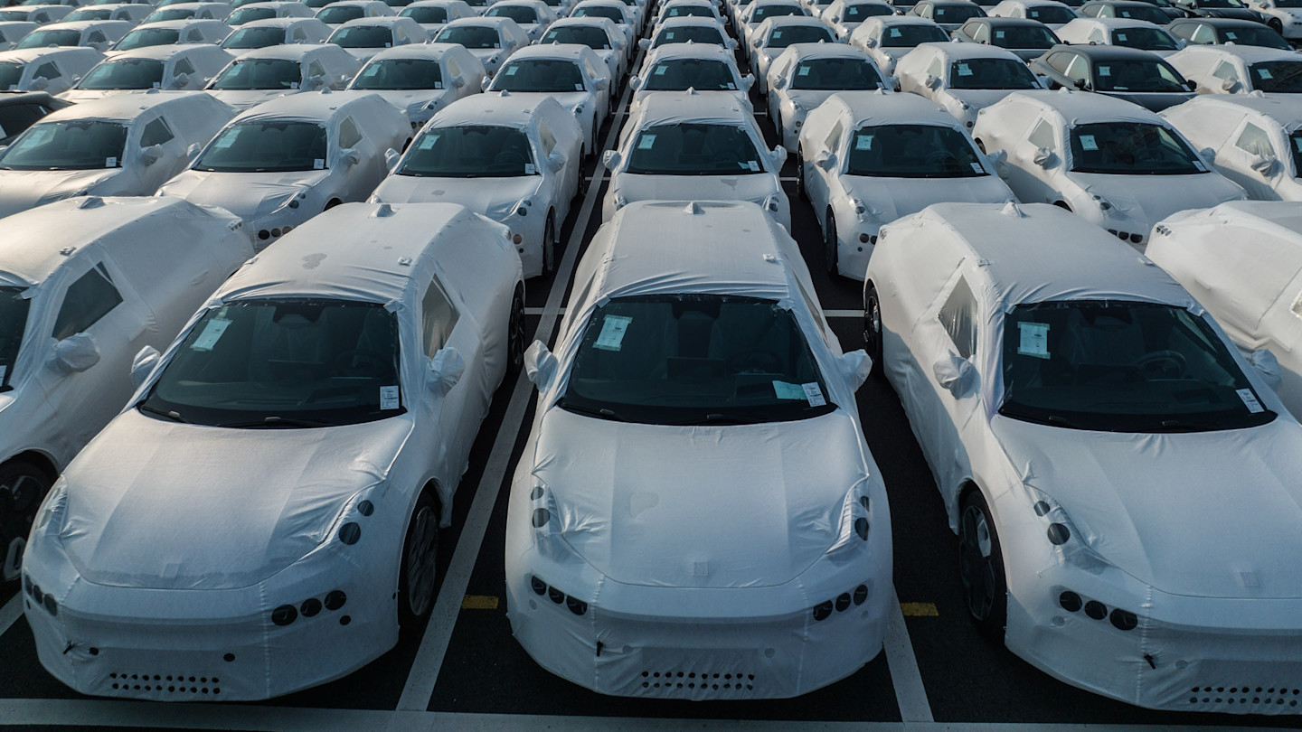 Rows of Geely Zeekr electric vehicles covered in protective white wrapping, parked closely together at a port, prepared for shipment