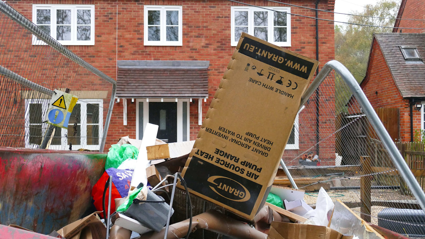 A cardboard box labelled ‘air source heat pump’ and other waste in a skip outside a newly built brick house.