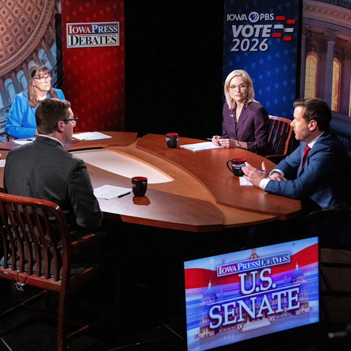 Ashley Hinson and Josh Turek sit at a table with a moderator during the debate