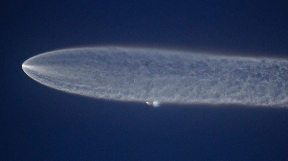 A SpaceX Falcon 9 rocket leaves a bright, wide trail of vapor in the evening sky after launch, seen from a distance.