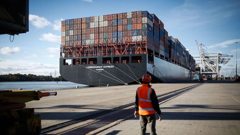 A worker in a safety vest and helmet stands on the dock as the Ludwigshafen Express container ship arrives at the Port of Southampton