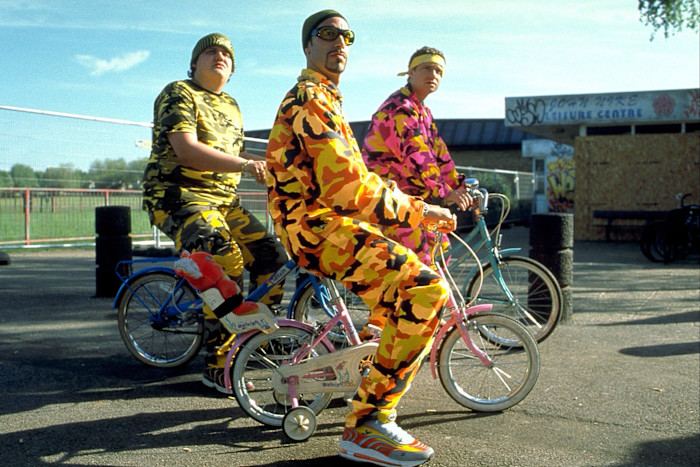 Tony Way, Sacha Baron Cohen as Ali G, and Martin Freeman wear brightly colored camouflage outfits and ride bikes in a scene from “Ali G Indahouse.”