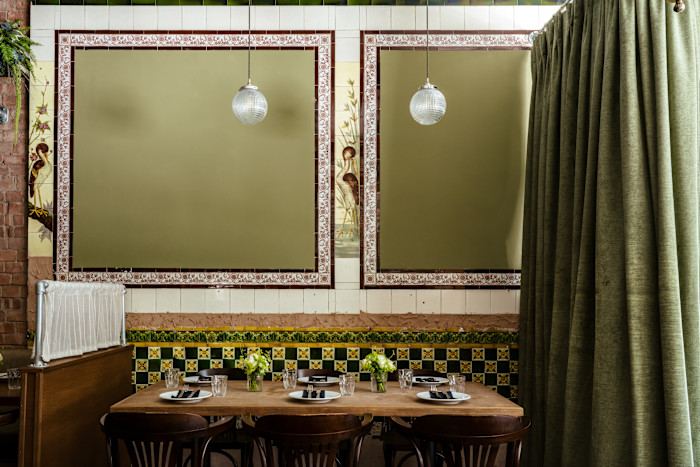 A restaurant interior with green velvet seating, framed wall panels and heavy curtains.