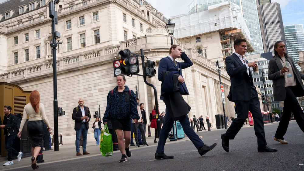 Office workers and pedestrians cross a street in front of the Bank of England building in London’s financial district.