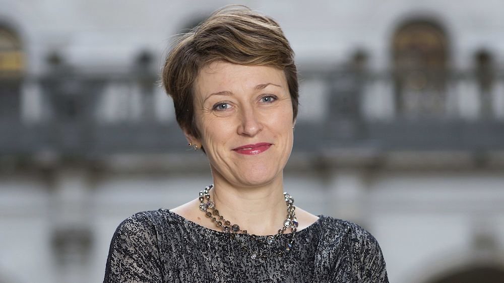 Katharine Braddick poses smiling at the Bank of England, wearing a patterned top and a beaded necklace.