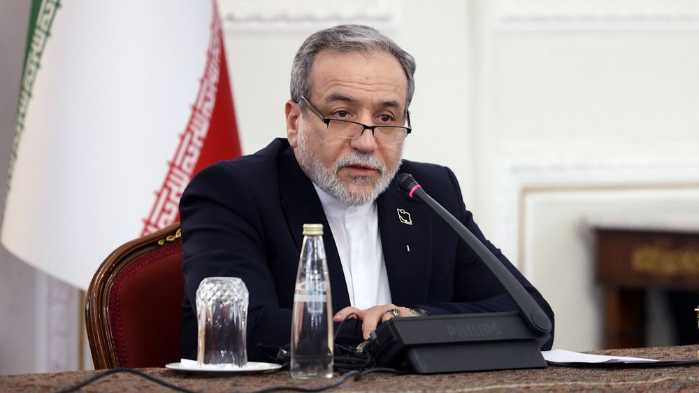 Abbas Araghchi speaks into a microphone at a press conference, seated at a table with a glass and water bottle.
