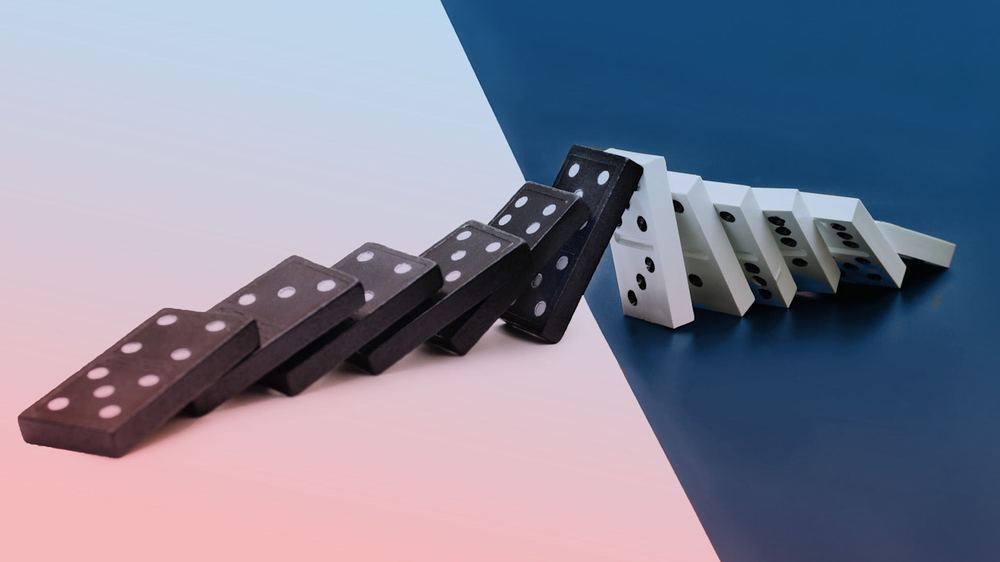 A row of black dominoes tipping into a row of white dominoes, all falling across a divided background.