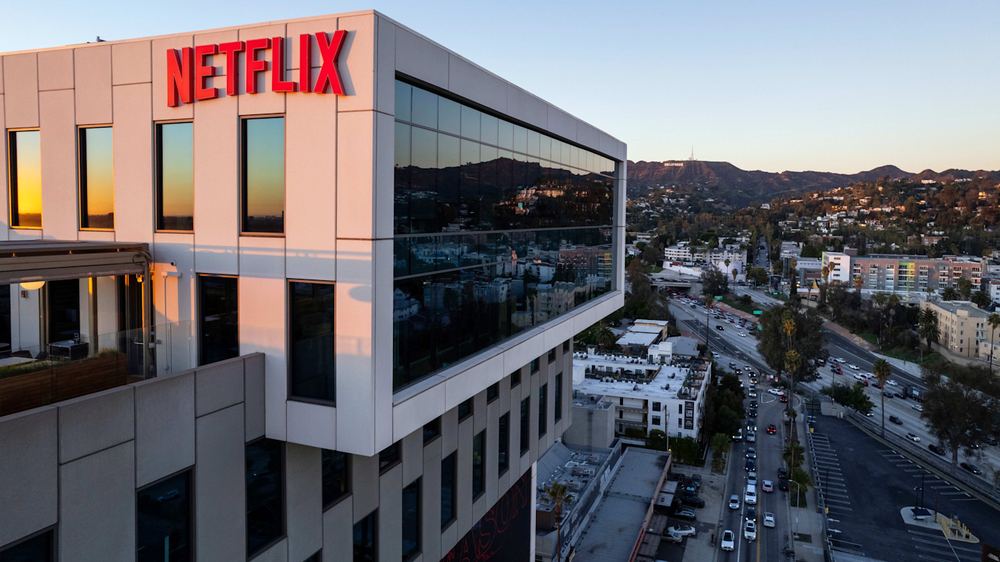 Netflix headquarters building with the red Netflix logo, overlooking Los Angeles with the Hollywood sign visible in the distance.