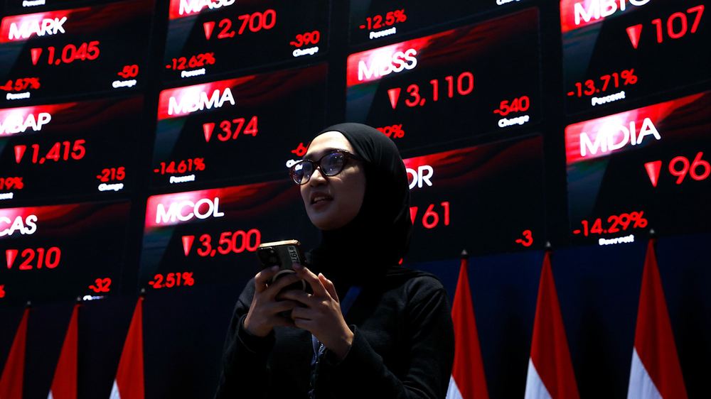 A woman stands in front of an electronic board showing steep declines in stock prices at the Indonesia Stock Exchange.