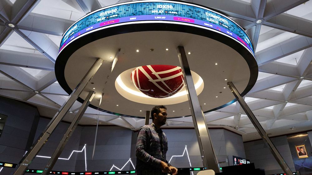 A man walks past a large circular electronic board displaying stock market figures inside the Indonesia Stock Exchange in Jakarta.