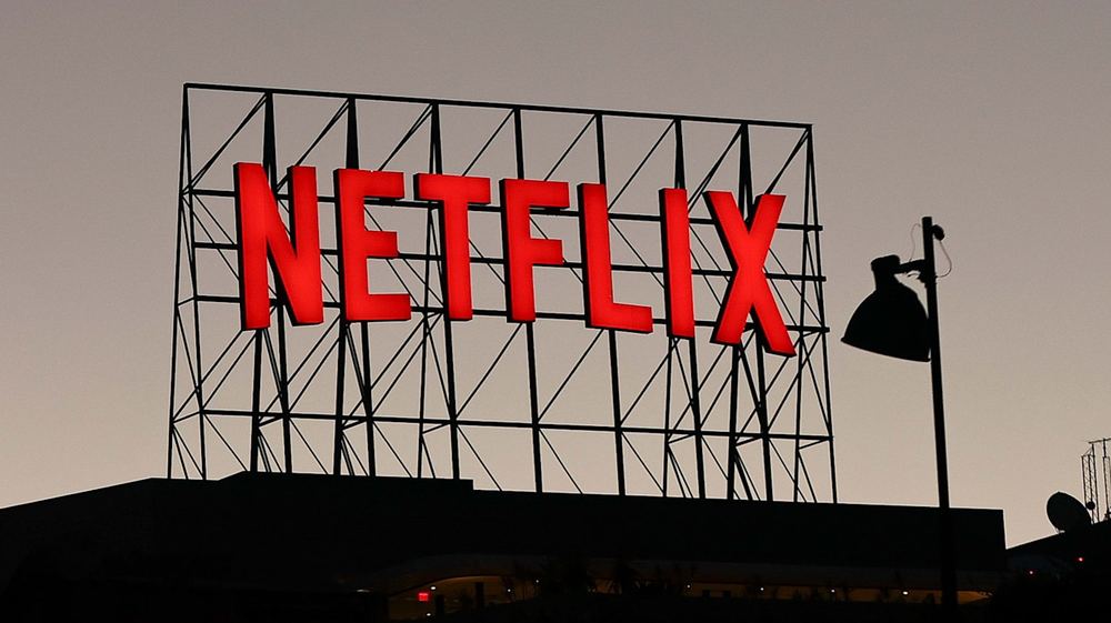 Large red Netflix logo sign mounted on the roof of an office building at dusk.