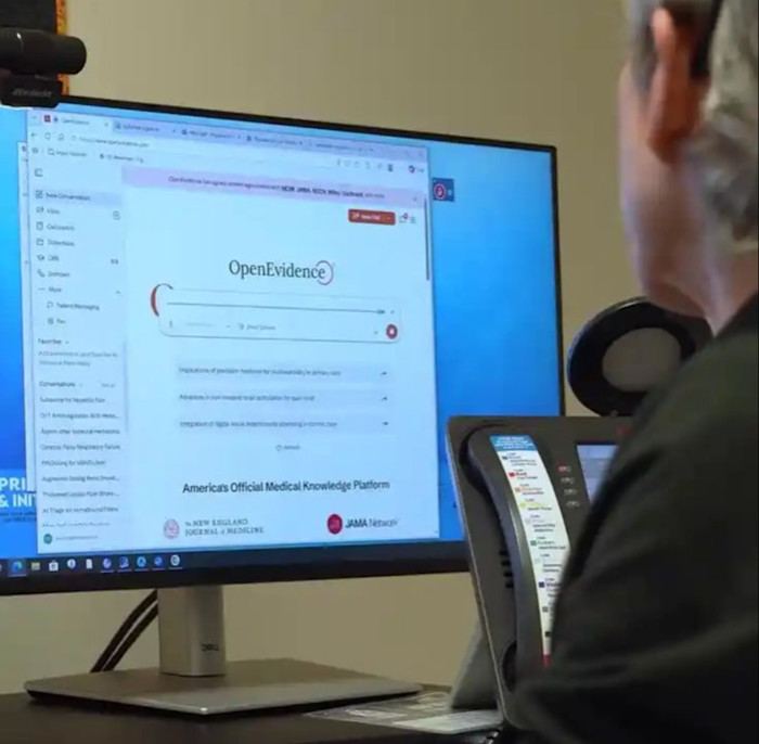 A person sits at a desk using a computer displaying the OpenEvidence medical knowledge platform.