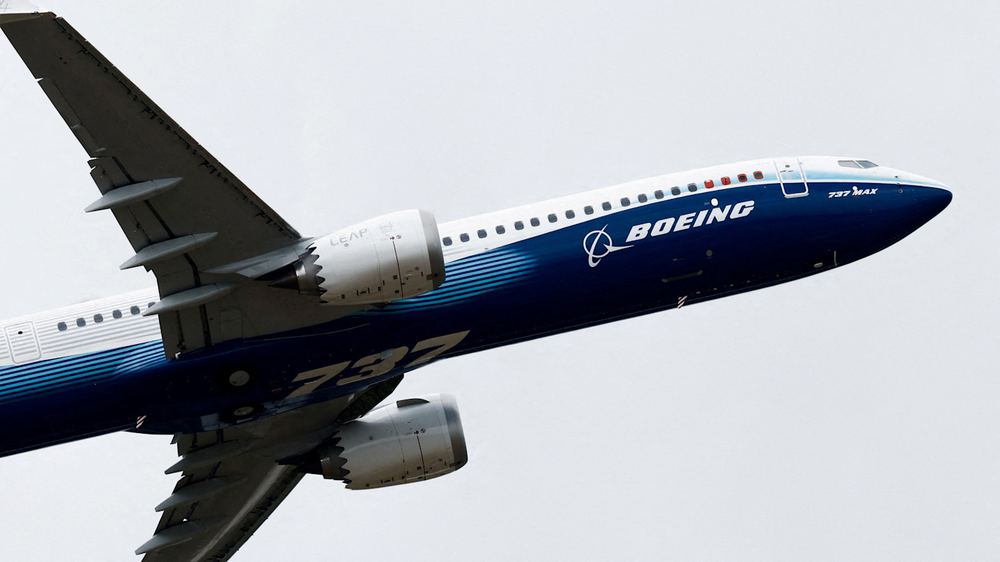 A Boeing 737 MAX-10 aircraft in flight, shown from below with its landing gear retracted.