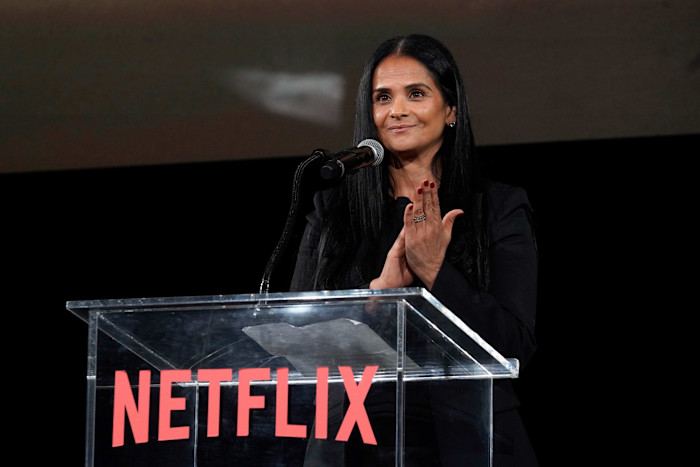 Bela Bajaria stands at a podium with a microphone, speaking onstage at a Netflix premiere event.