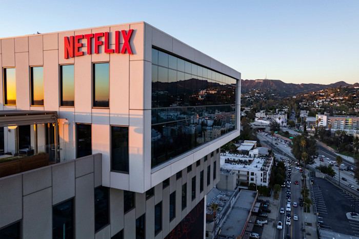 Netflix headquarters building with large red Netflix sign, city streets below, and the Hollywood Hills in the distance.