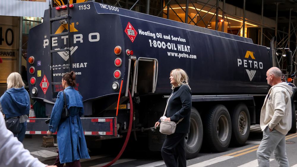 A heating oil truck with "PETRO" branding is parked on a city street as several pedestrians walk by.