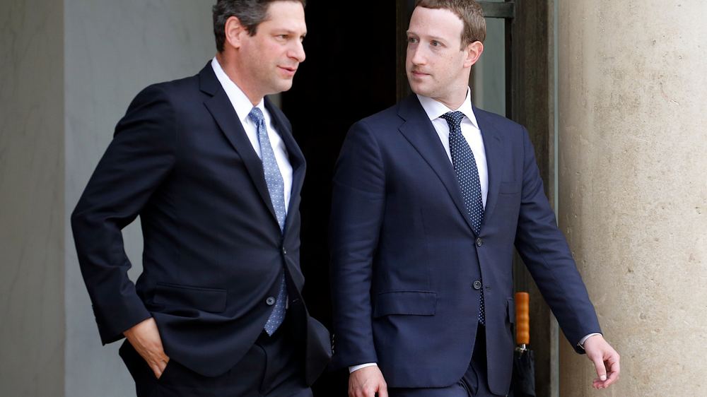Joel Kaplan and Mark Zuckerberg walk together in suits after leaving a building, looking at each other.
