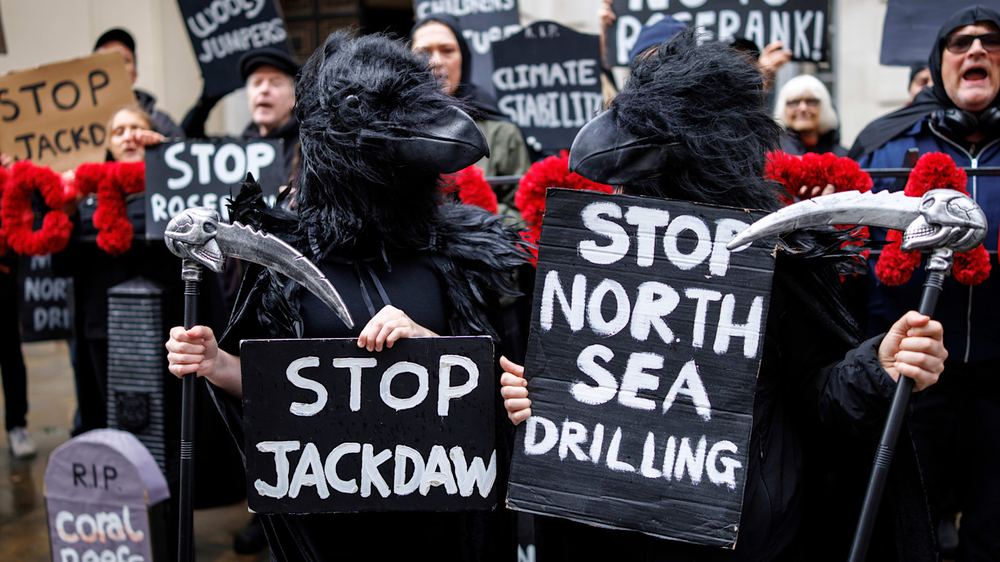 Climate protesters in black bird costumes hold signs reading "Stop Jackdaw" and "Stop North Sea Drilling" at a demonstration.
