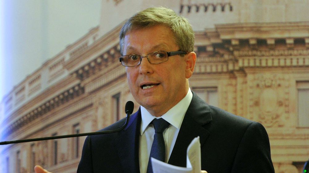 Gyorgy Matolcsy speaks at a podium, holding papers during a press conference at the Hungarian Central Bank headquarters.