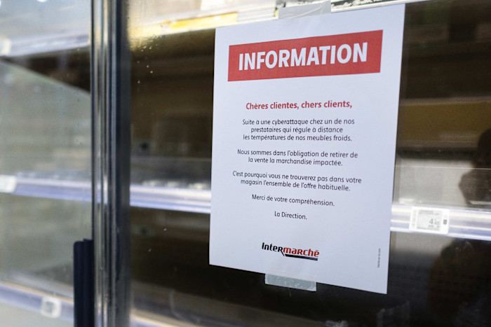 A customer notice explaining a cyber attack is posted on empty fresh-food refrigerator shelves at an Intermarché supermarket