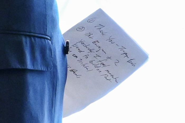 A close-up shows a handwritten note in English held by a person in a blue suit.