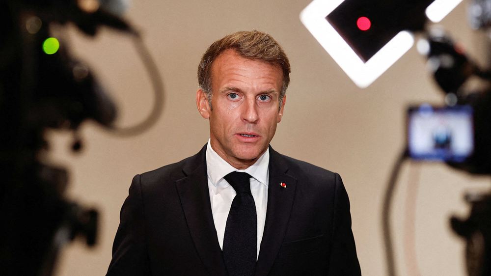 Emmanuel Macron speaks to the media, framed by cameras and lighting equipment, during the OPSWF Summit.