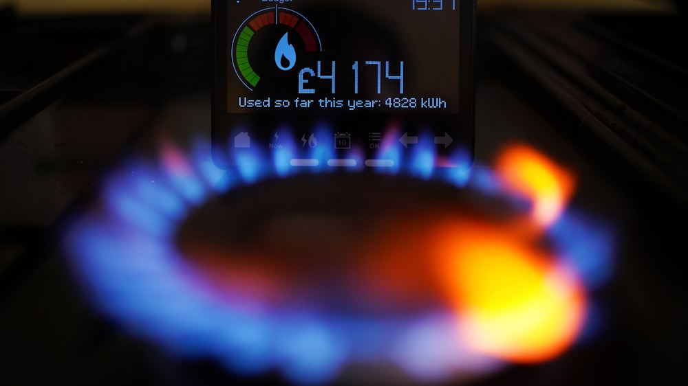 A smart meter displaying £4,174 spent and 4,828 kWh used this year, positioned behind a lit gas hob burner.