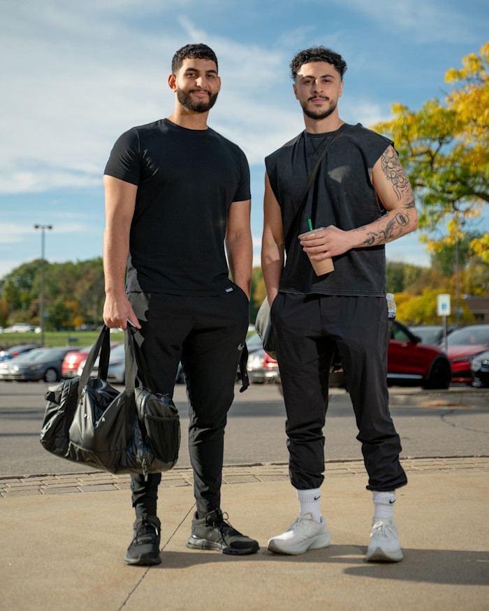 Mohammed Awadalla and Hussein Ajami stand outside Fairlane Mall, both dressed in black athletic wear and looking at the camera.