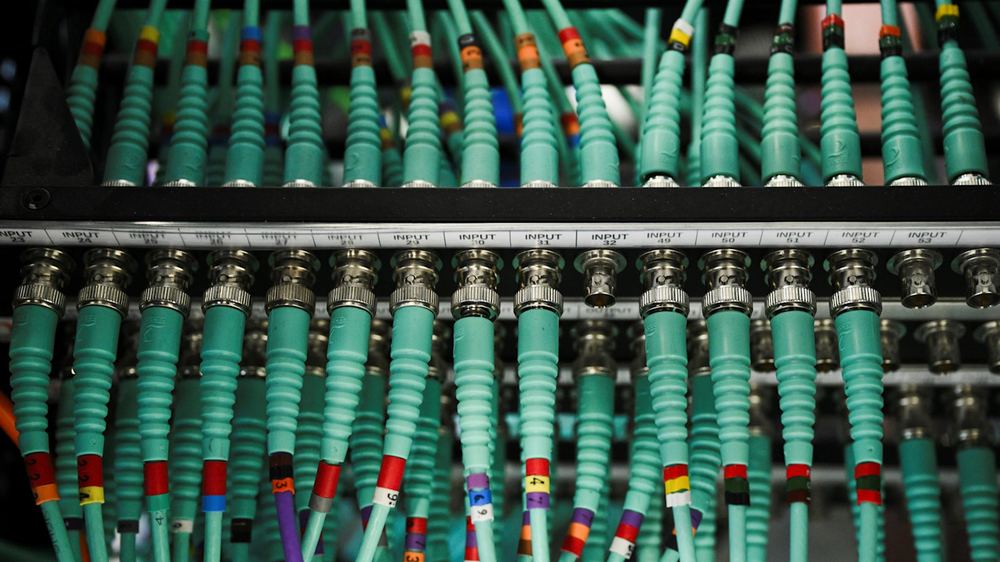 A row of teal network cables plugged into labeled input ports on a computer server, with colored bands marking each cable.